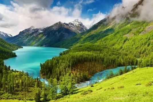 जंगल और हरी ढलानों से घिरी फ़िरोज़ी रंग की पहाड़ी झील